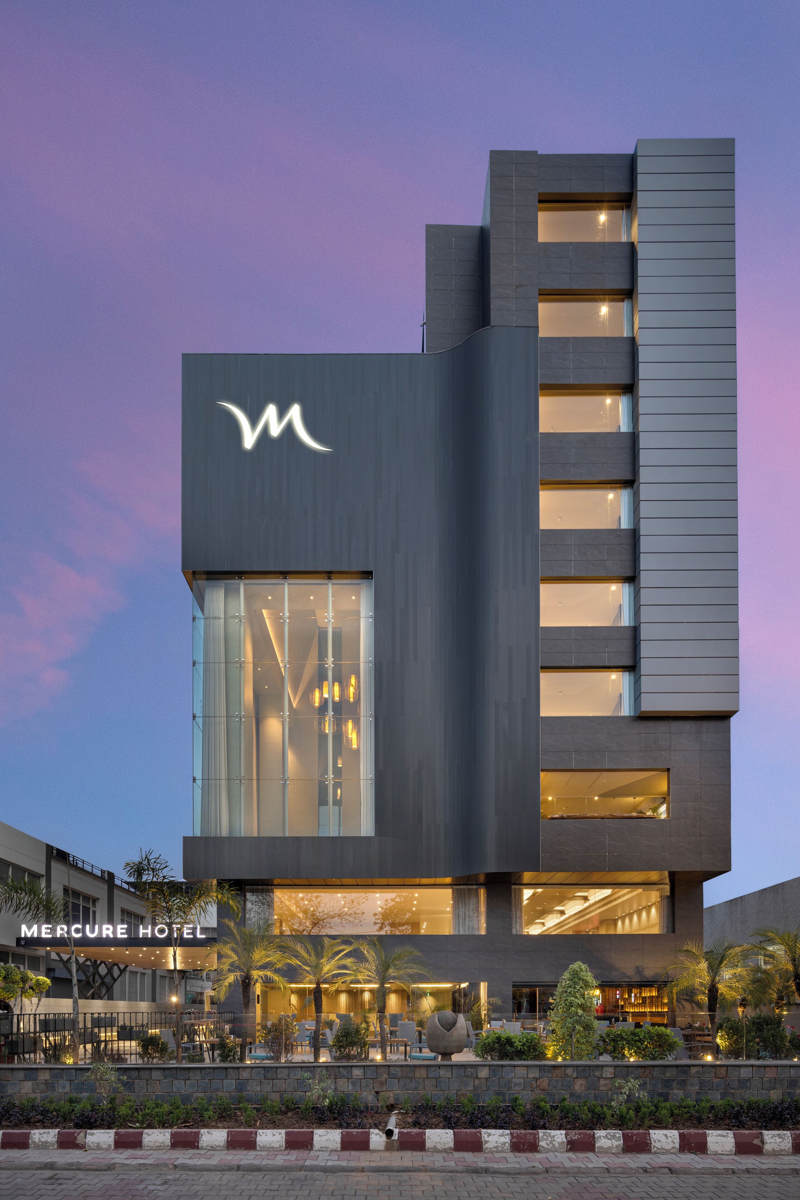 A modern hotel with a prominent 'M' logo, large windows, and a well-lit lobby area.