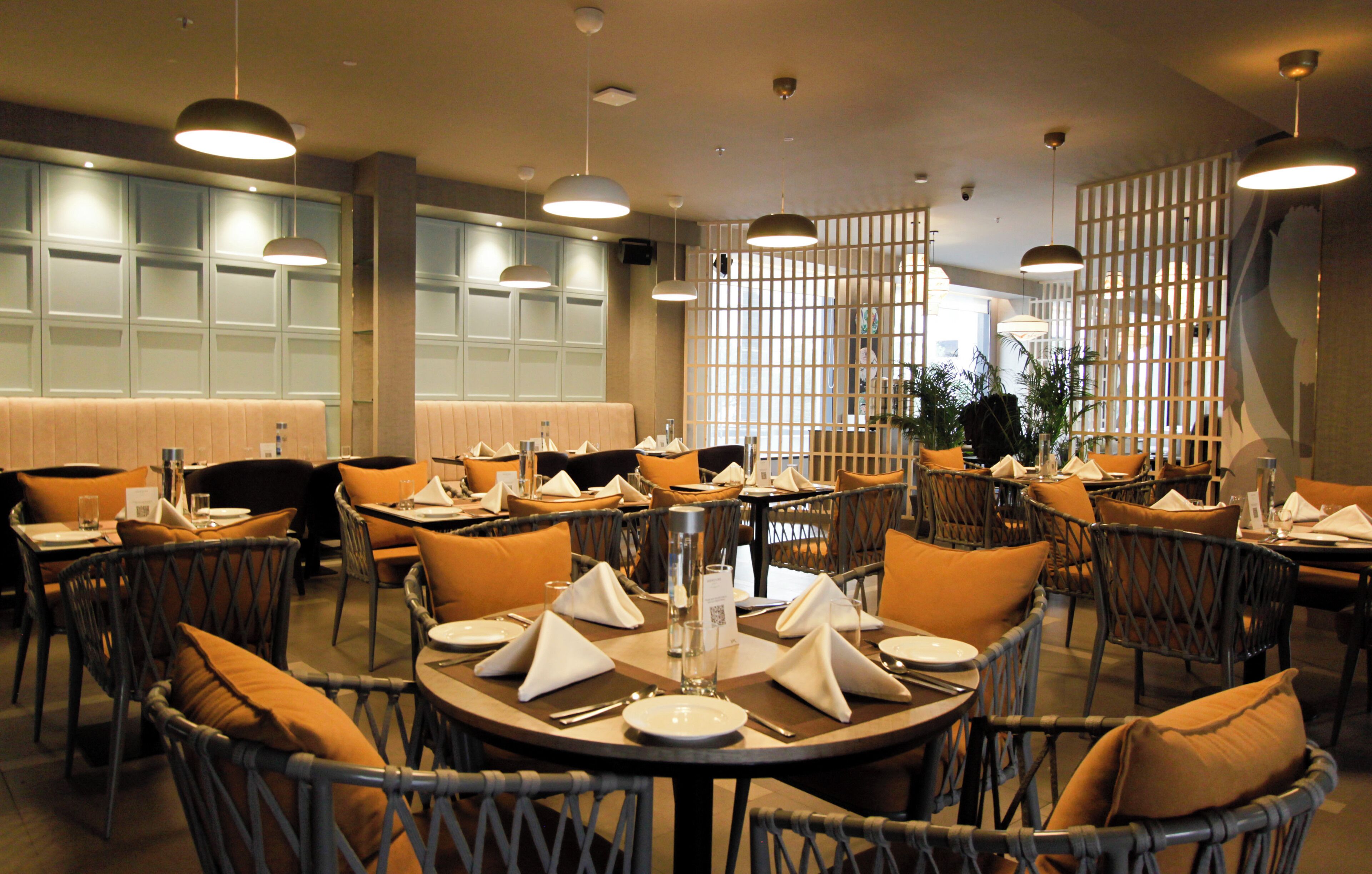 A restaurant with round tables, wicker chairs, and orange cushions.