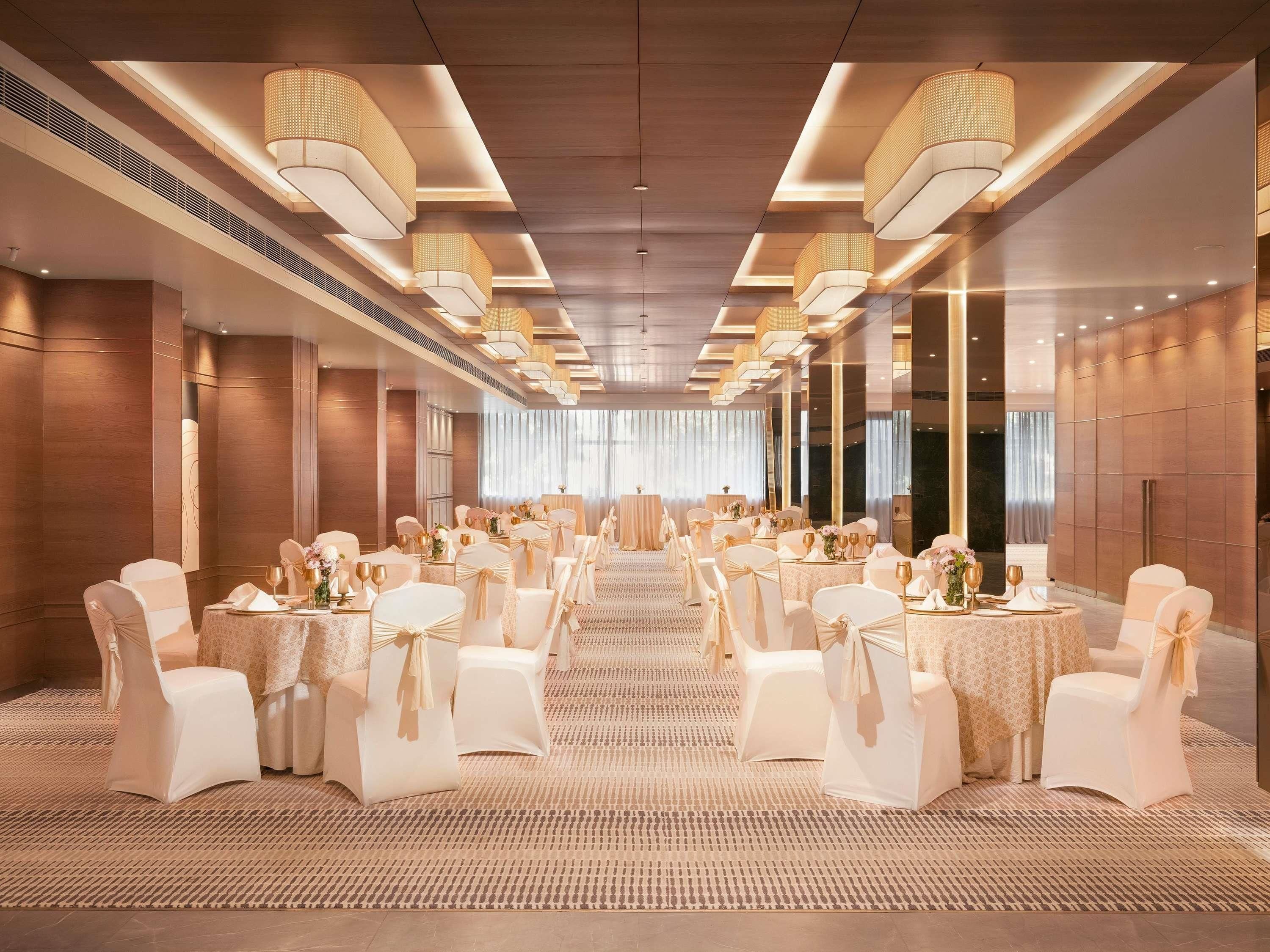 A banquet hall with round tables, white chairs, and chandeliers.