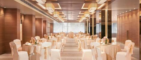 A banquet hall with round tables, white chairs, and chandeliers.