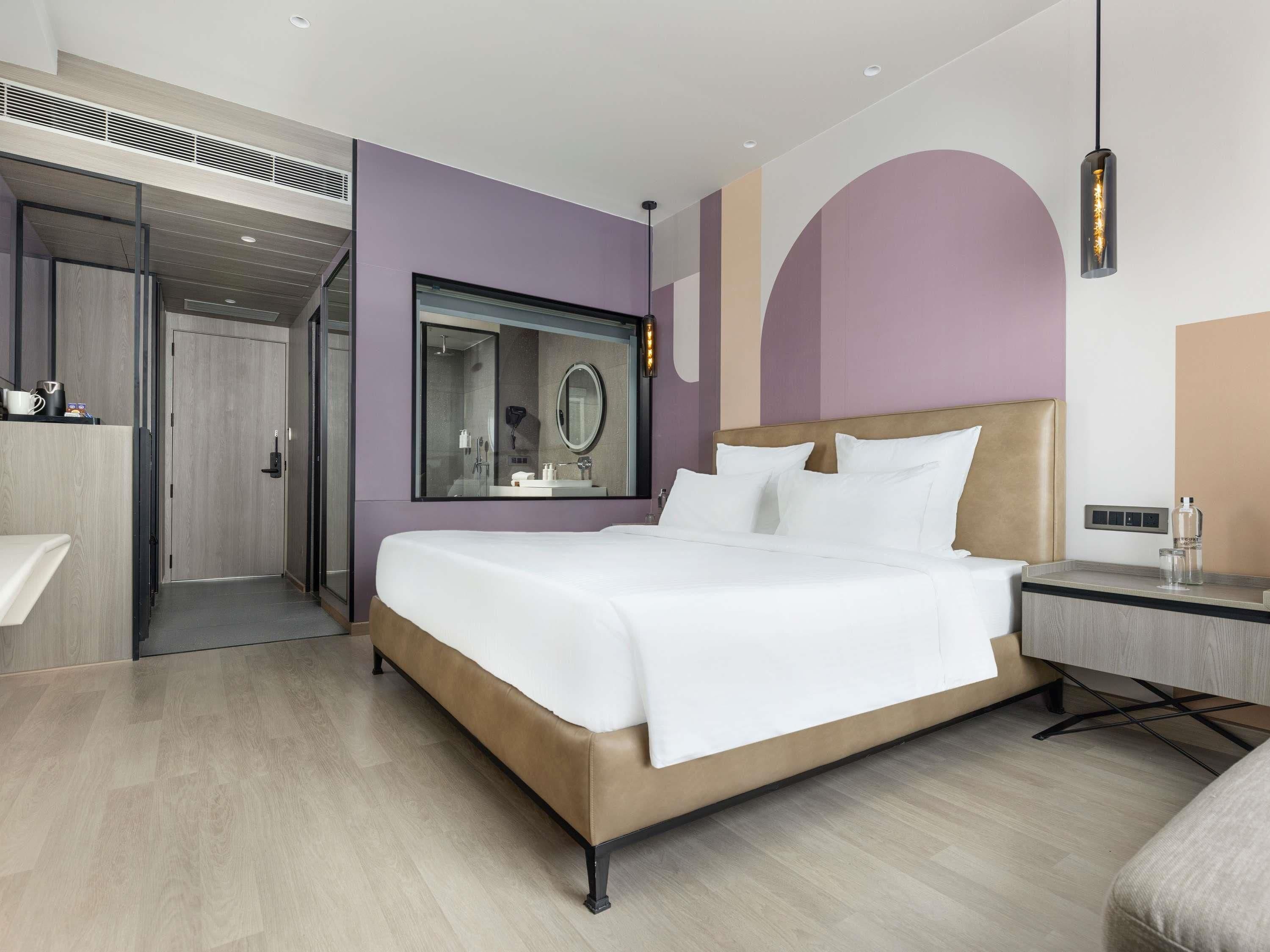 A modern hotel room with a large bed, a vanity with a mirror, and a nightstand.