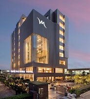 Un hotel moderno con un llamativo letrero de 'Mercure Hotel', grandes ventanales y una terraza en la azotea con mobiliario exterior.