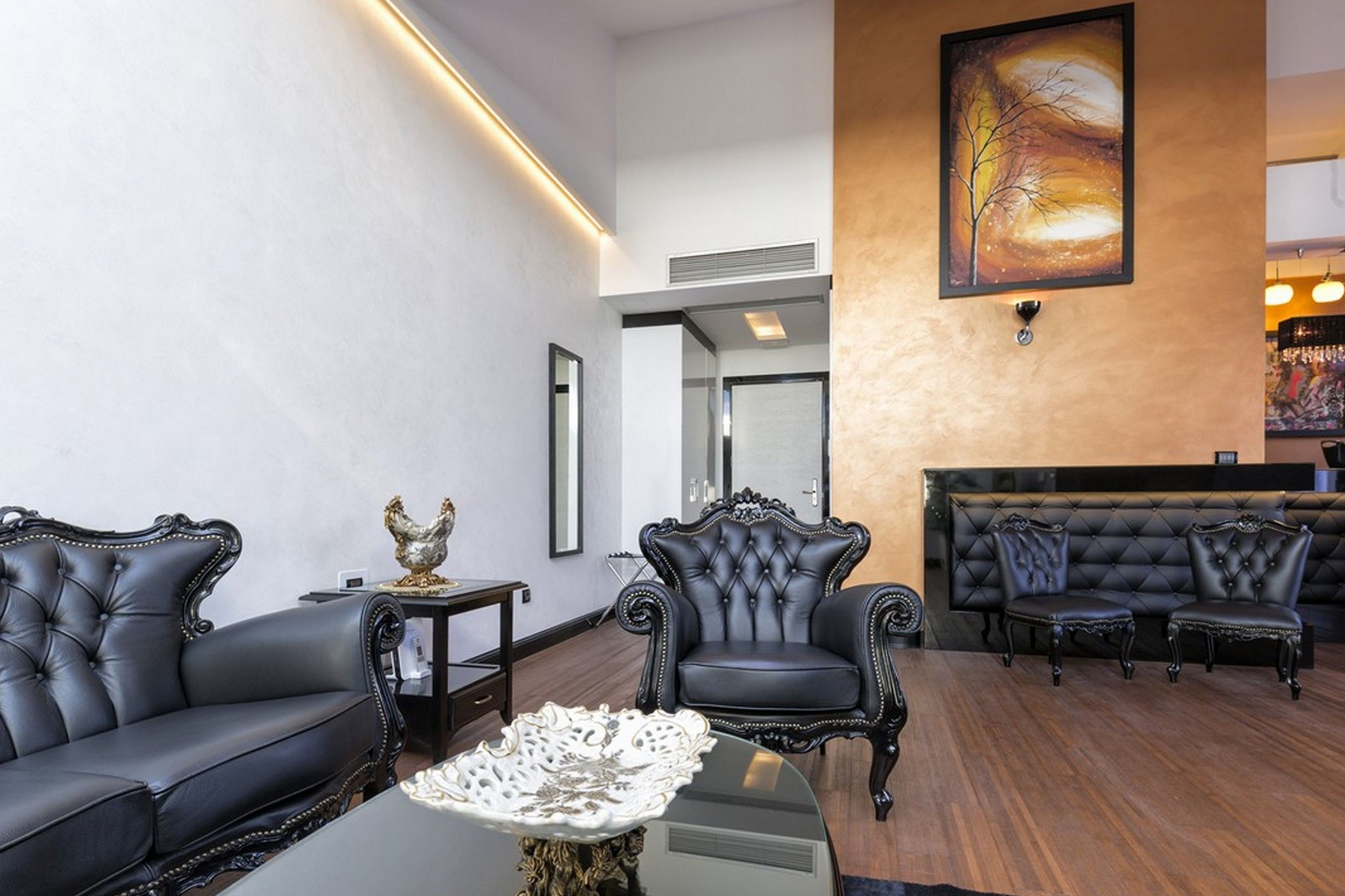 A spacious lobby with a black leather sofa, a tufted armchair, and a seating area with black leather chairs.