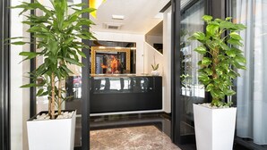 Un área de recepción con piso de mármol, un mostrador de recepción y dos plantas grandes en macetas.
