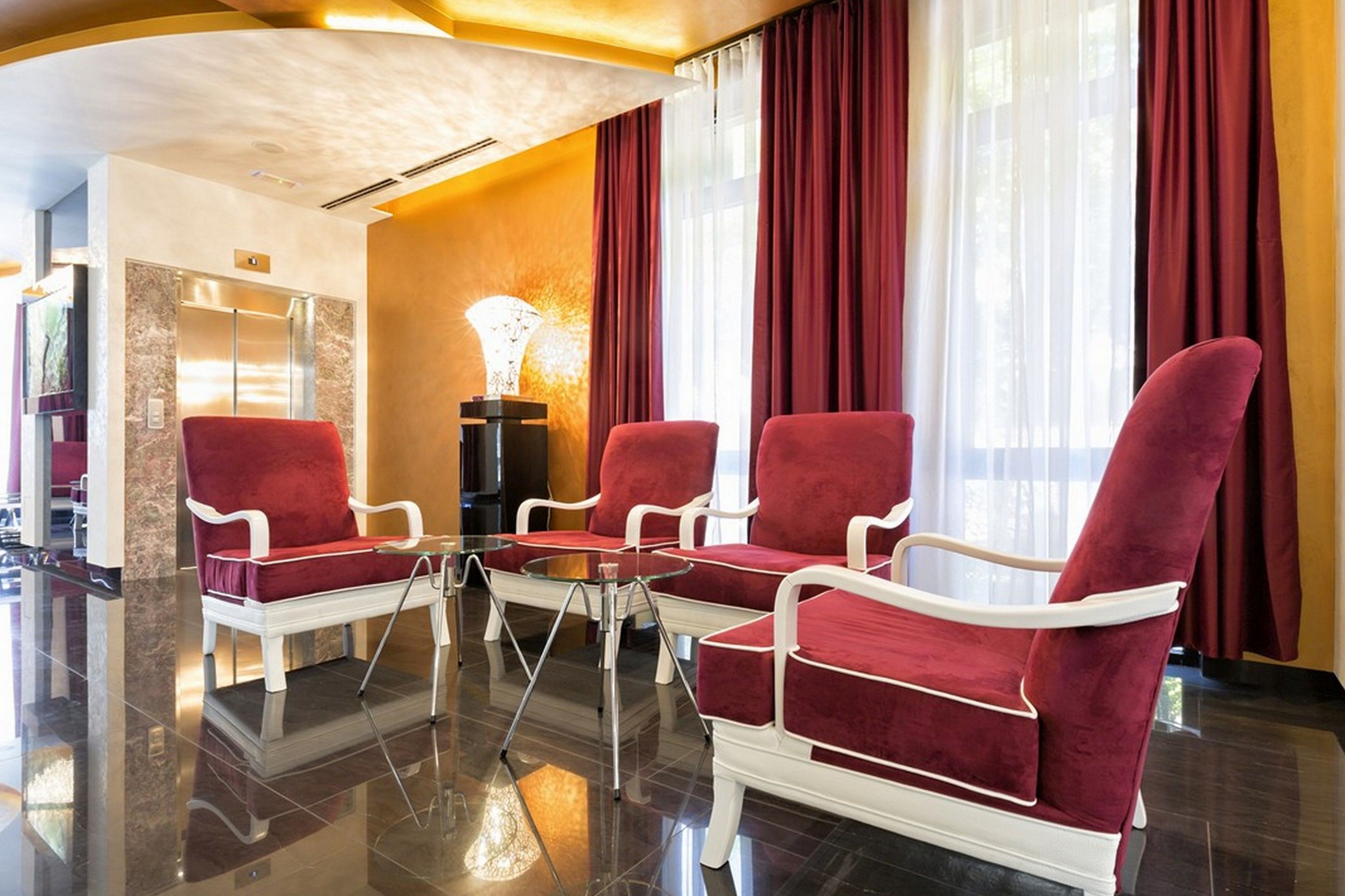 Un hall amb quatre seients tapissats de color vermell, una taula de cafè de vidre i una recepció de marbre.