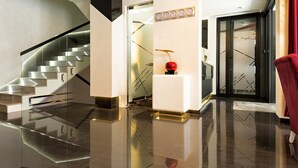 Un vestíbulo de hotel moderno con una escalera de cristal, una escultura esférica roja y un sillón rojo.