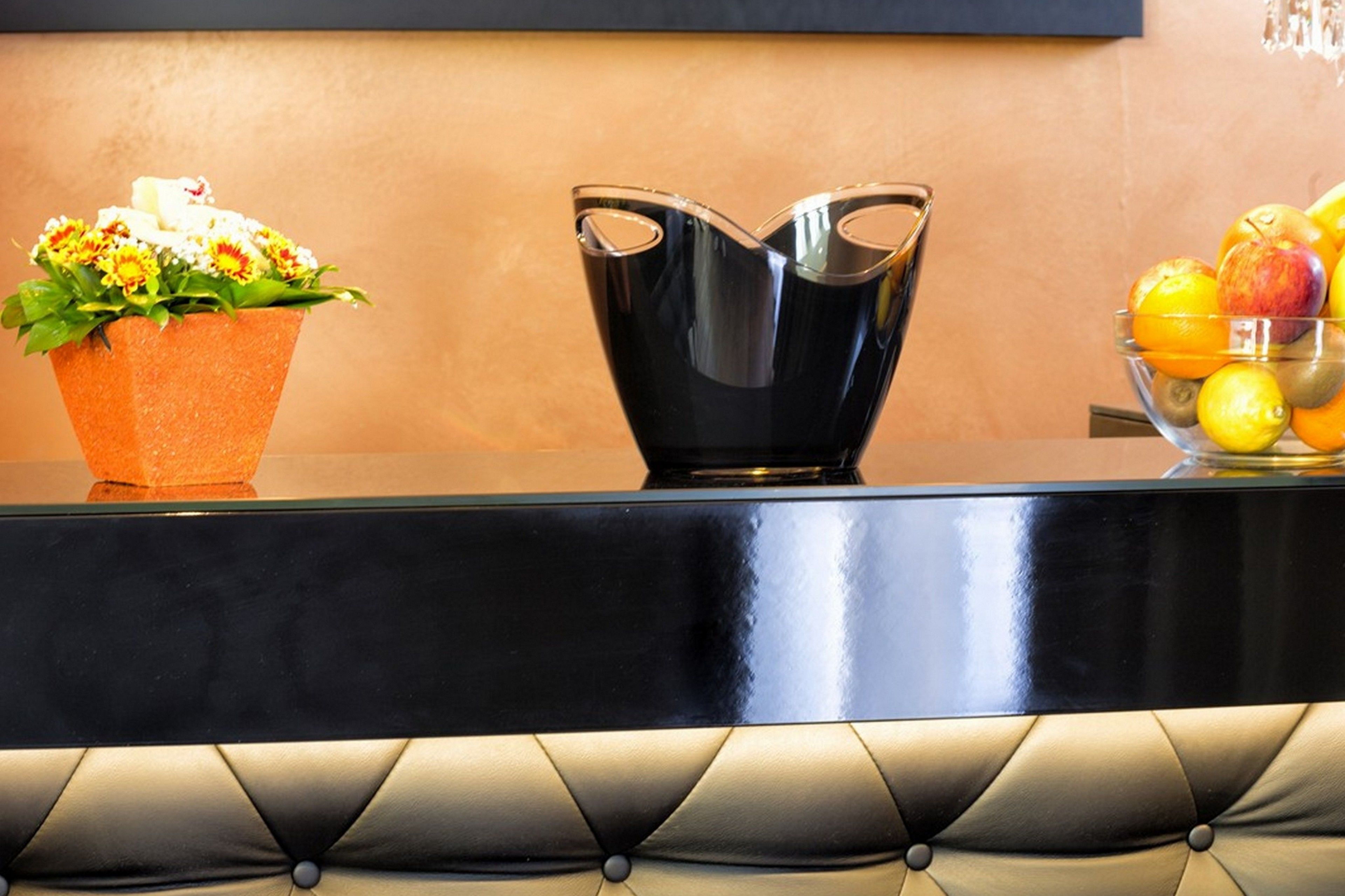 A reception area with a black cushioned bench, a glass vase with flowers, and a fruit bowl.