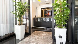 Un vestíbulo de hotel moderno con una recepción, plantas en macetas grandes y un piso de mármol.