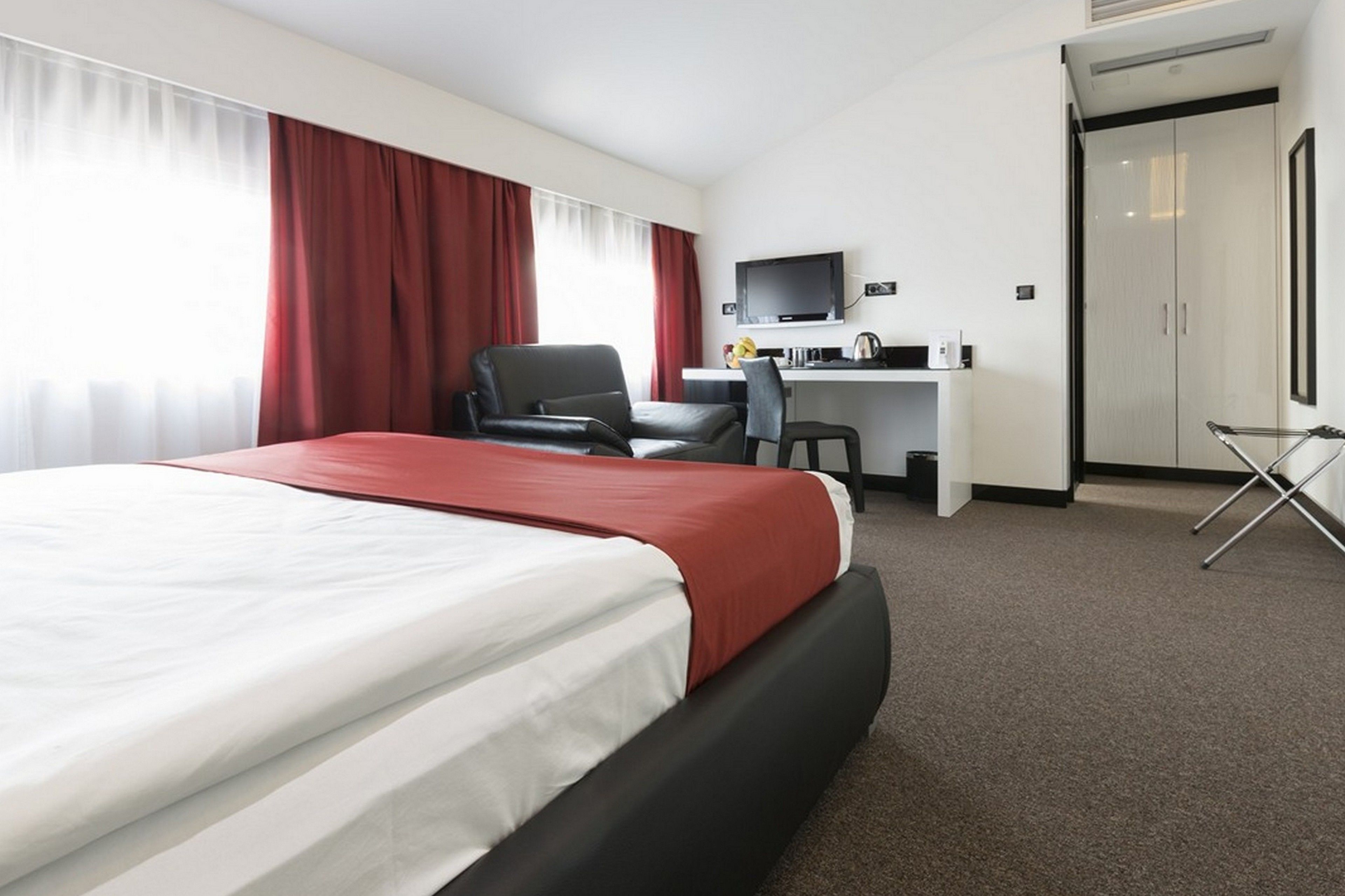 Una habitación de hotel con una cama grande, un escritorio con ordenador, una silla y un televisor.
