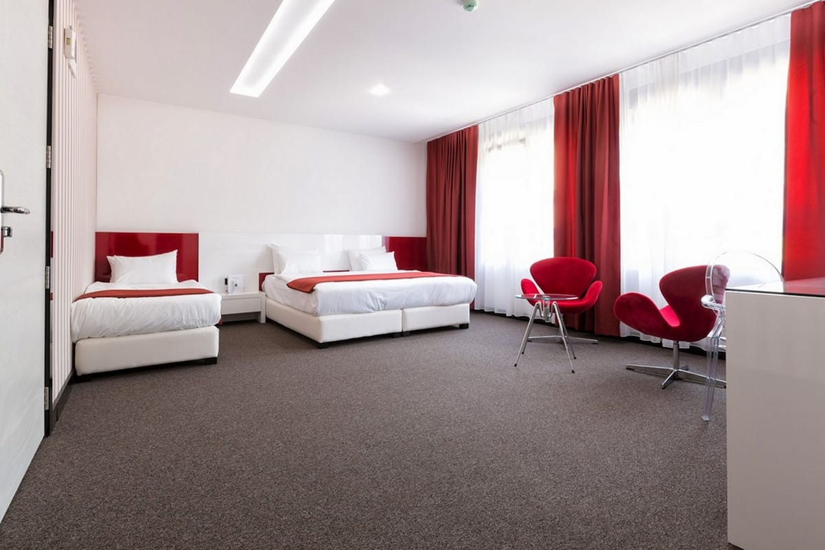 Quarto de hotel com duas camas, cadeiras vermelhas e uma mesa.