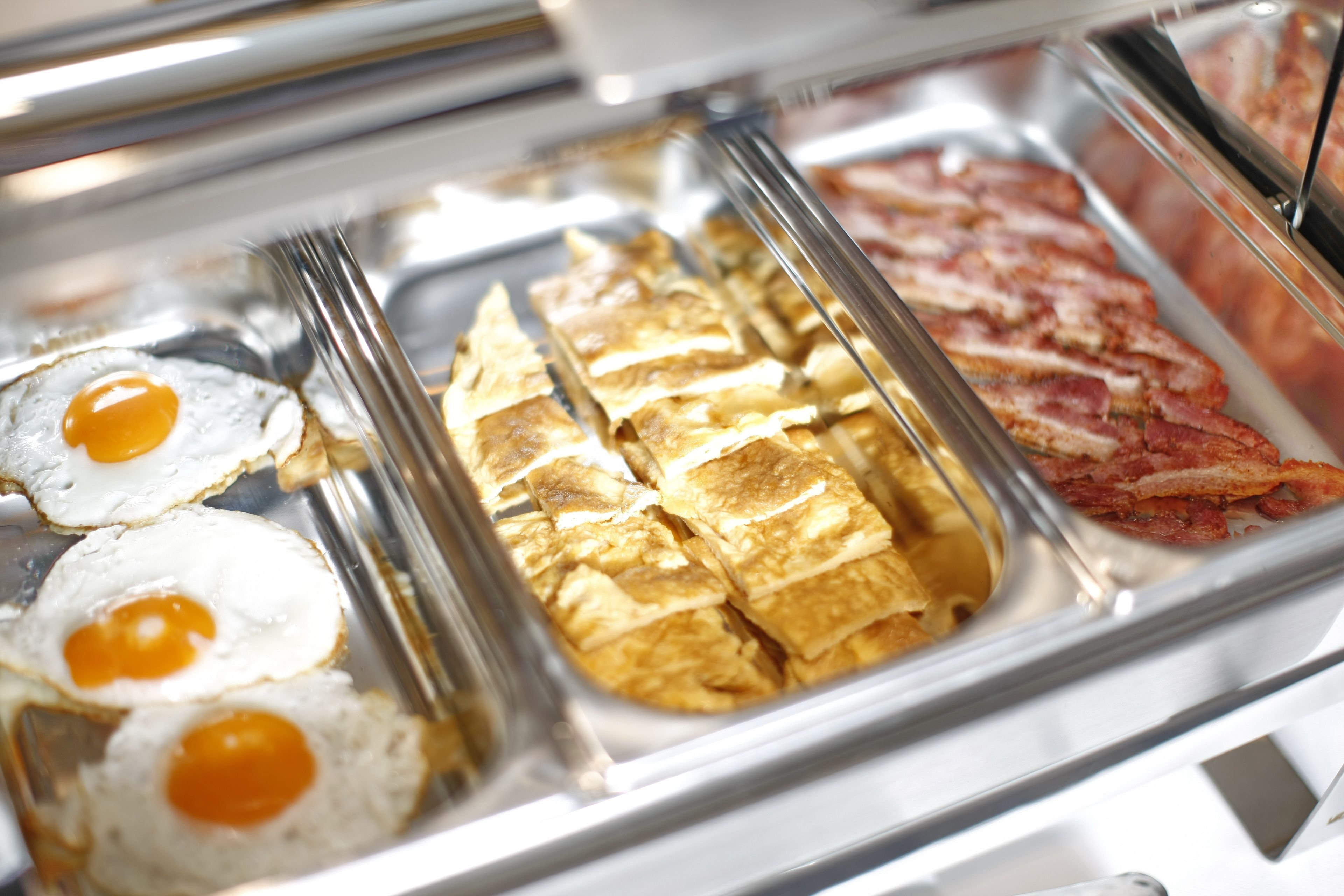 A breakfast buffet with fried eggs, omelets, and bacon.