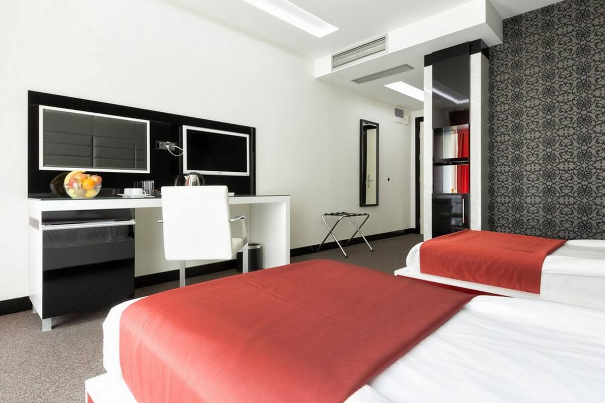 Quarto de hotel com cama, escrivaninha, cadeira, espelho e guarda-roupa.