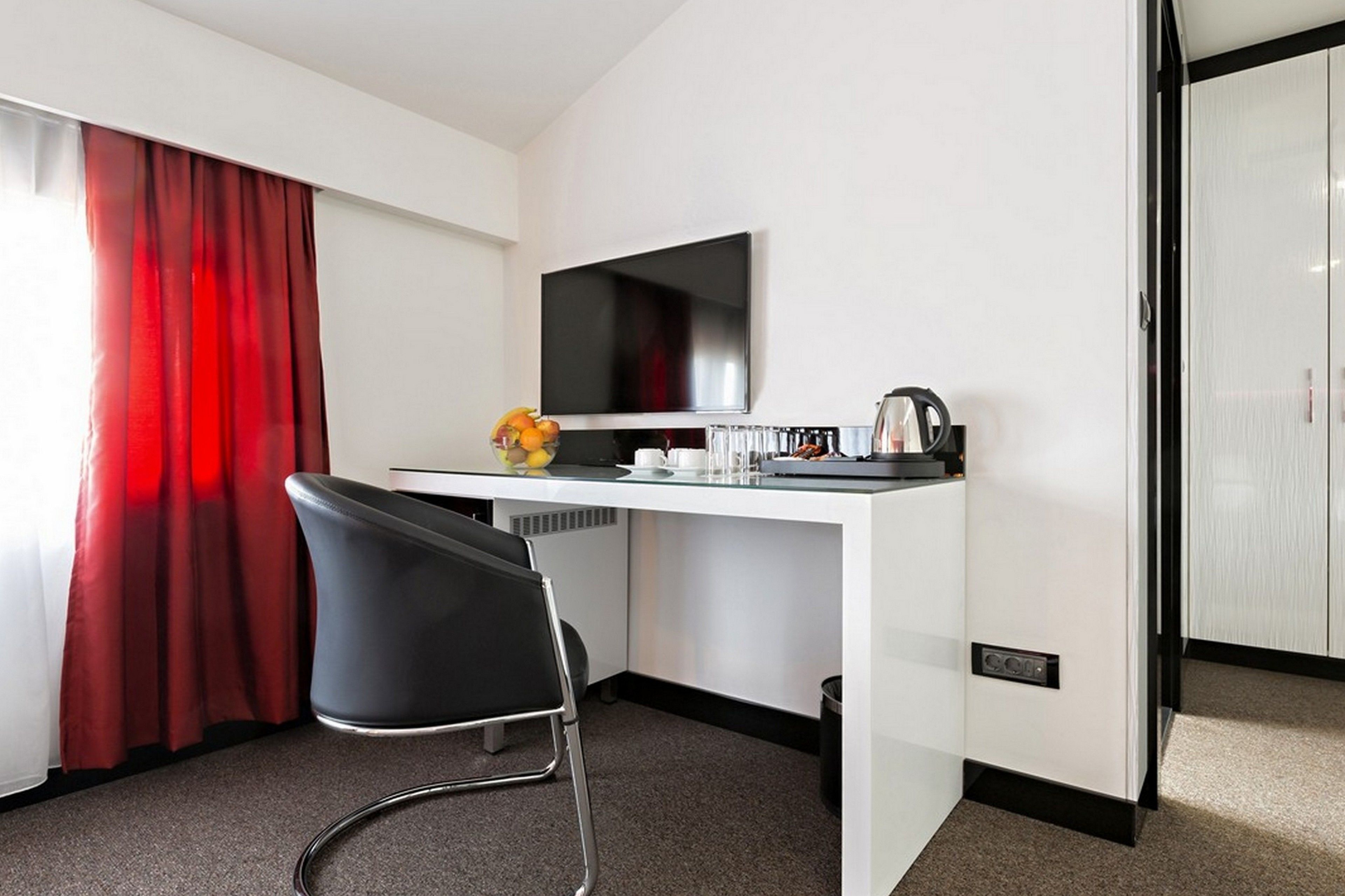A hotel room with a white desk, black chair, and a flat-screen TV.