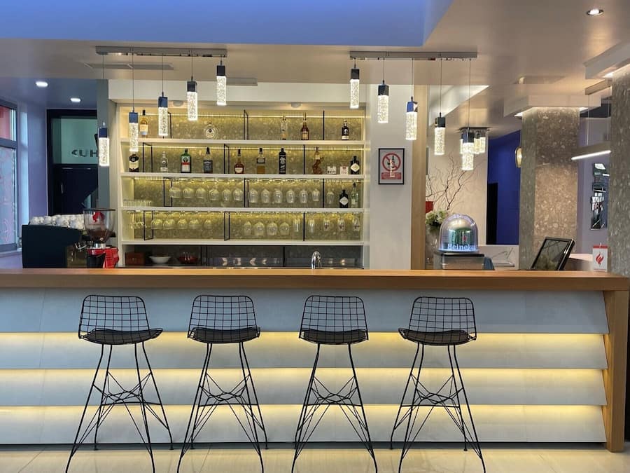 A modern bar area with a counter, bar stools, and shelves of liquor bottles.