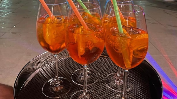 A poolside setting with a table holding four glasses of a beverage, each with a straw.