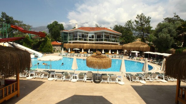 Ein Poolbereich eines Resorts mit Liegestühlen, Sonnenschirmen und einem Gebäude mit einem Reetdach.