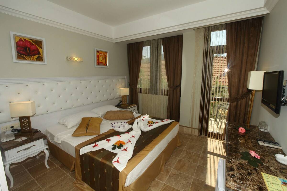 A hotel room with a large bed, a bedside table with a lamp, a television, and a window with curtains.