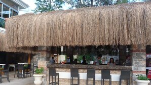 Ein Außenbereich mit Bar, ausgestattet mit Strohdach, Steinmauern und mehreren Barhocker.