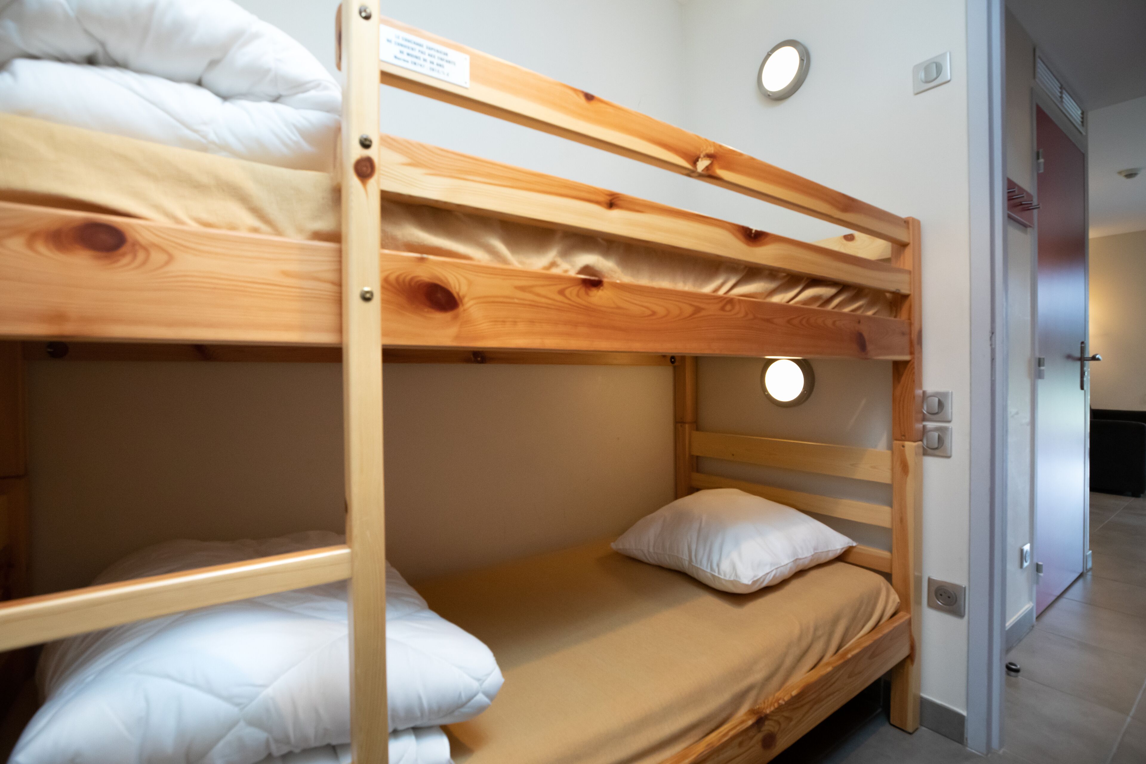 A bunk bed with a wooden frame and a single bed below. There is a white pillow on the lower bed and a white blanket on the upper bed.