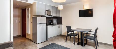 A compact kitchen with modern appliances, a dining area with a table and chairs, and a flat-screen TV mounted on the wall.
