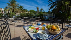 Een terras met tafels, stoelen en diverse gerechten, waaronder fruit, groenten en drankjes.
