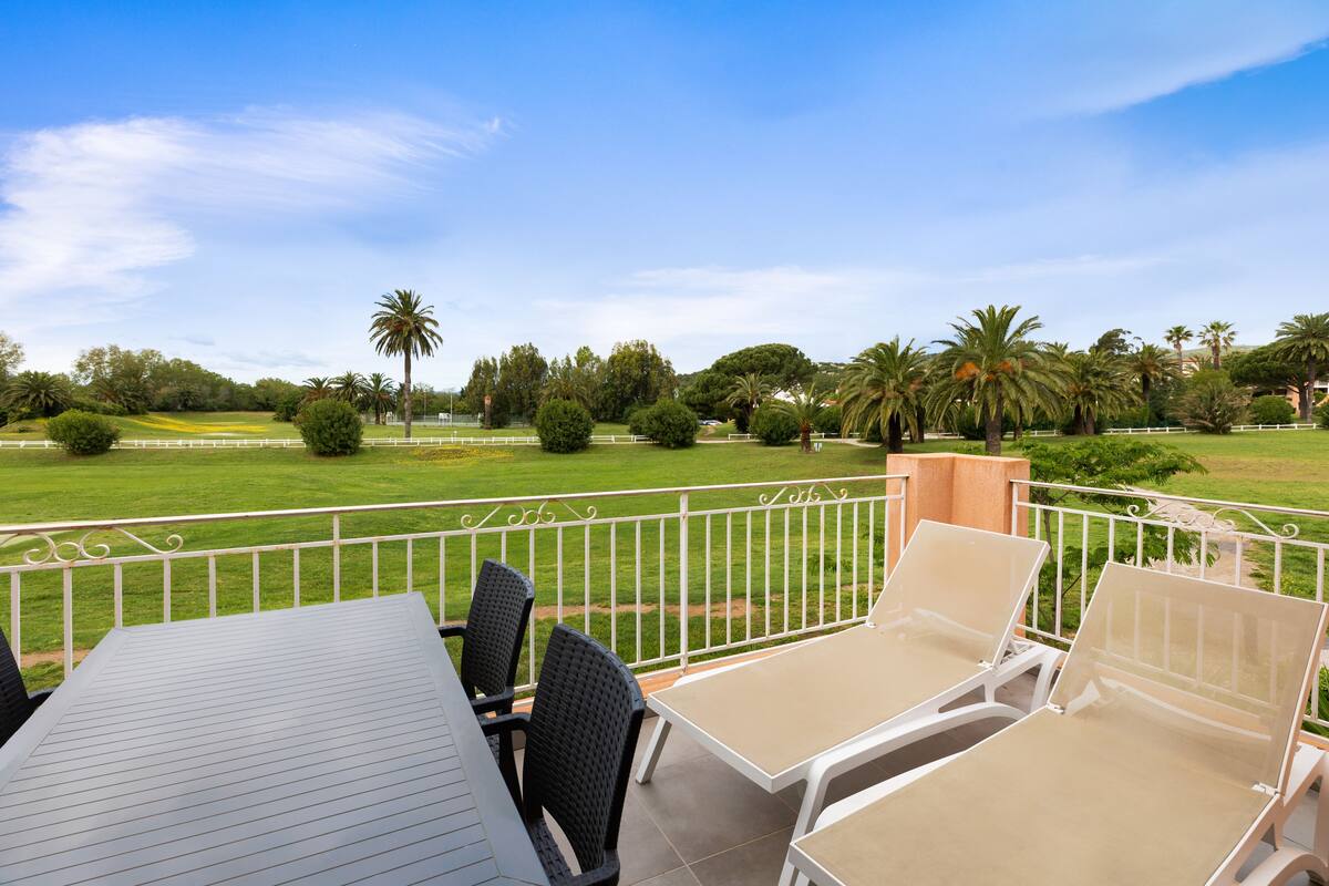 Un balcon avec une table et des chaises, donnant sur une pelouse bien entretenue et des palmiers.