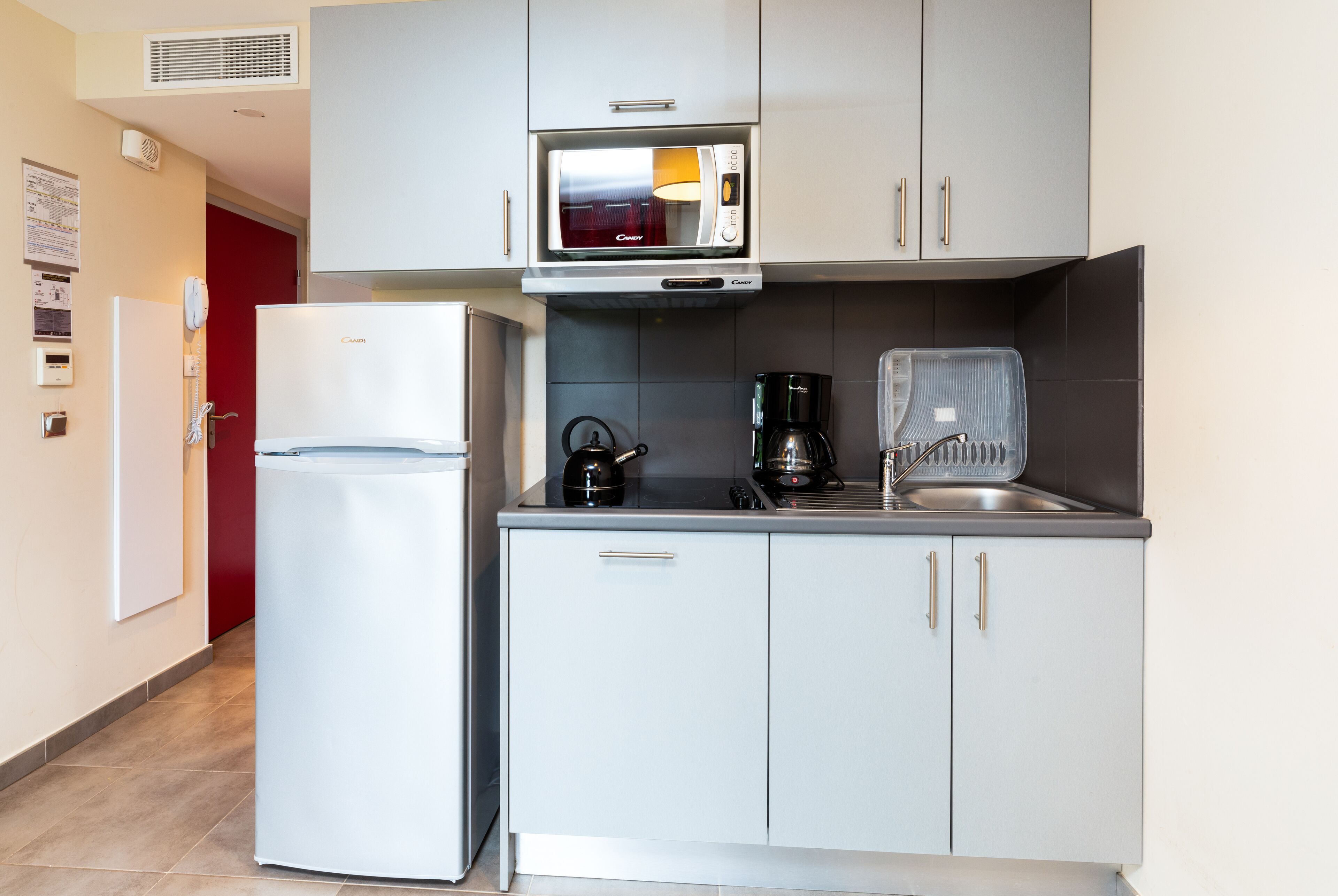 A compact kitchen with a white refrigerator, a microwave, a kettle, and a coffee maker.