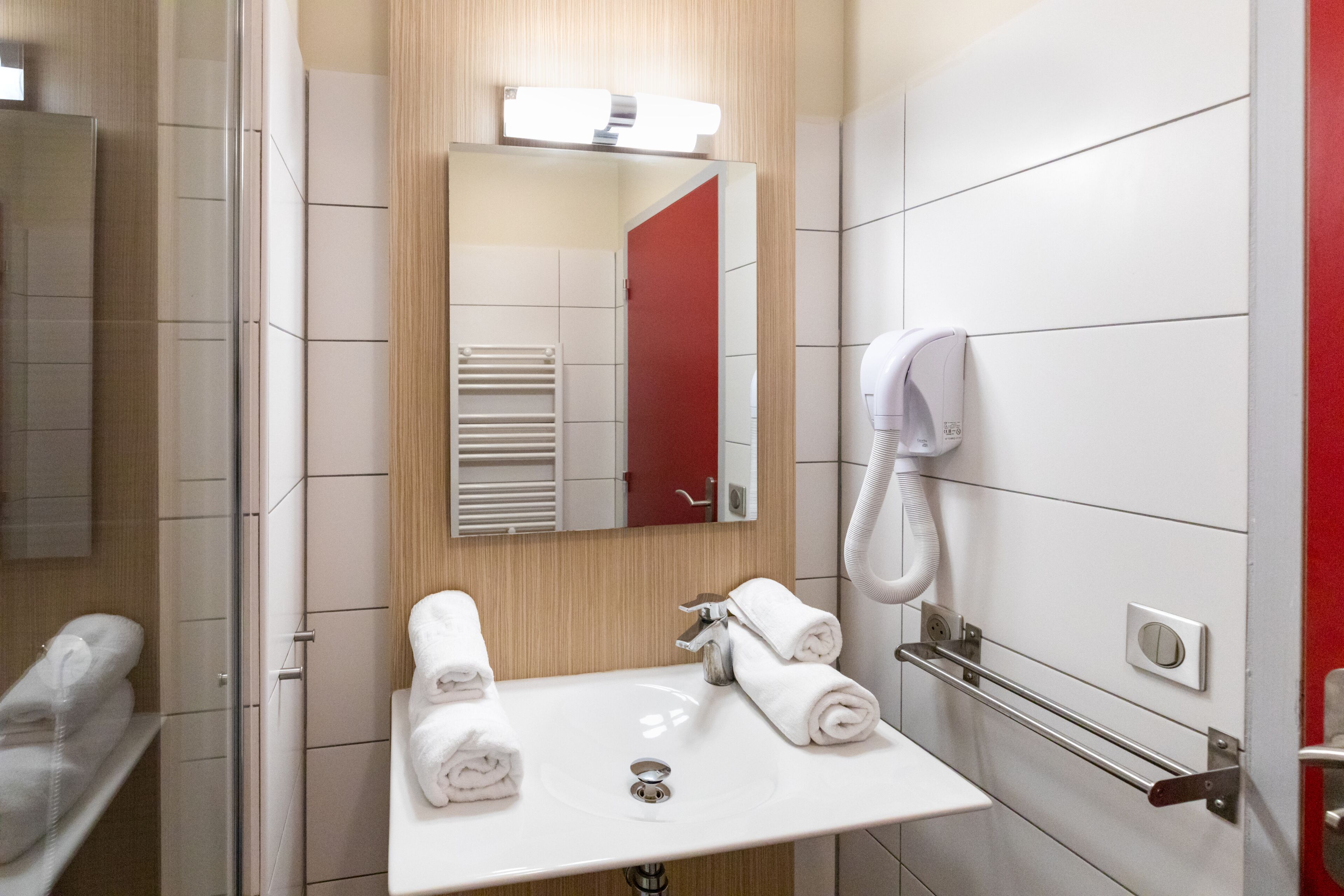 Une salle de bain moderne avec un lavabo blanc, un miroir, un porte-serviettes et un sèche-mains.