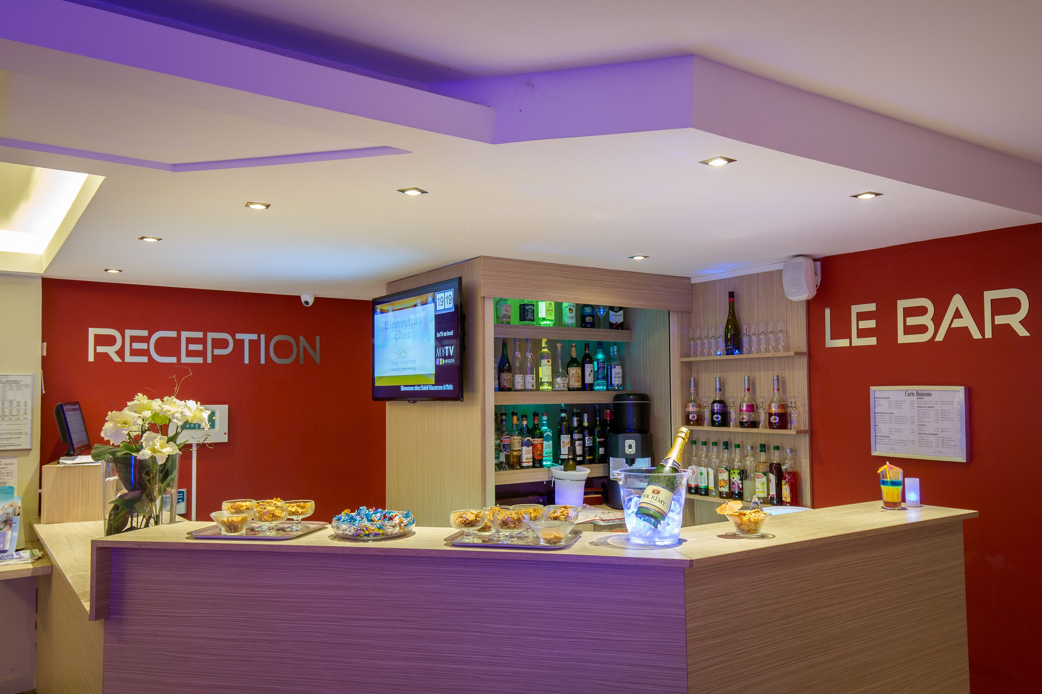 A reception area with a bar, a TV screen, and a variety of beverages and snacks.