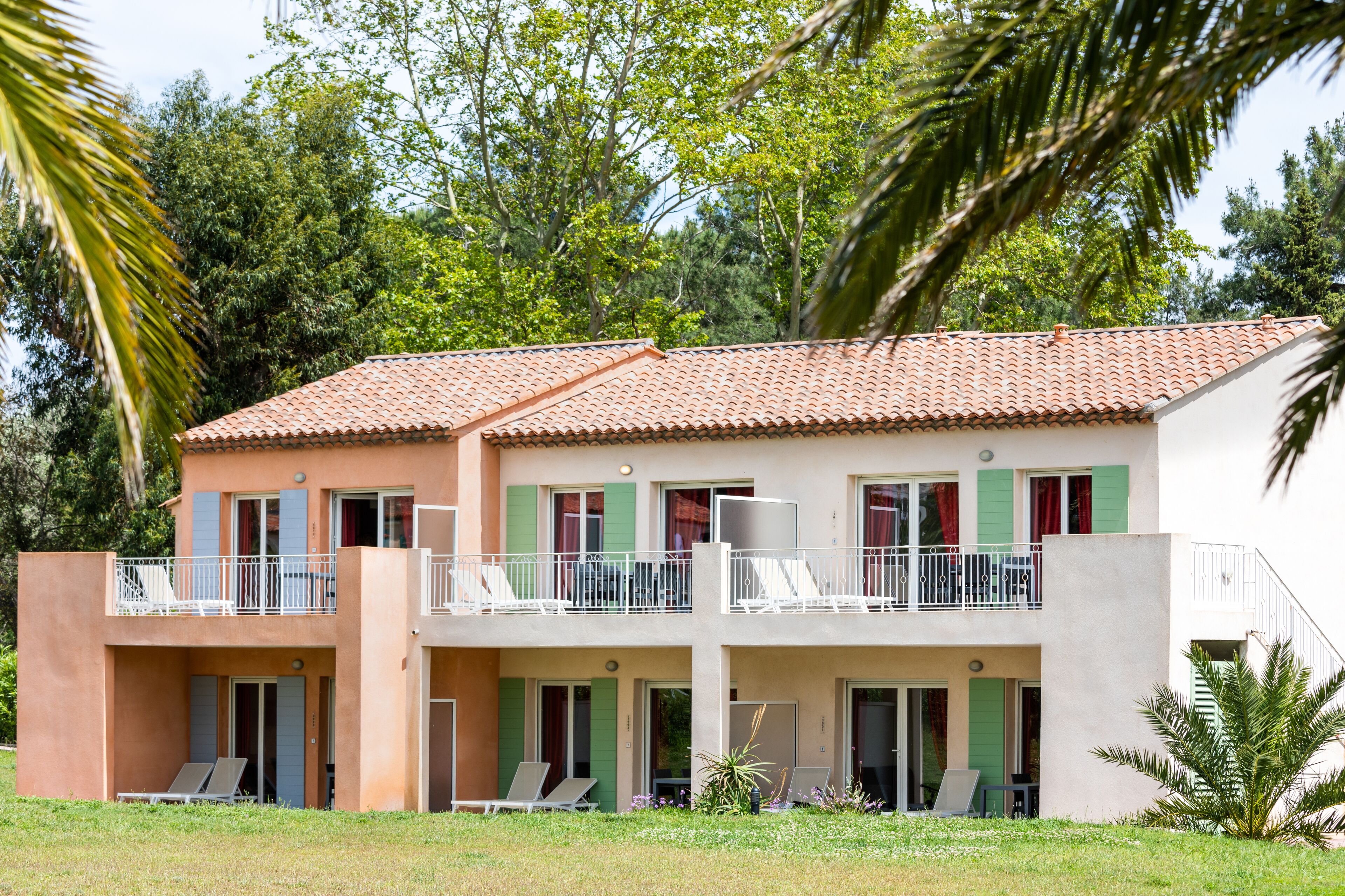 A two-story building with balconies, green shutters, and a tiled roof.