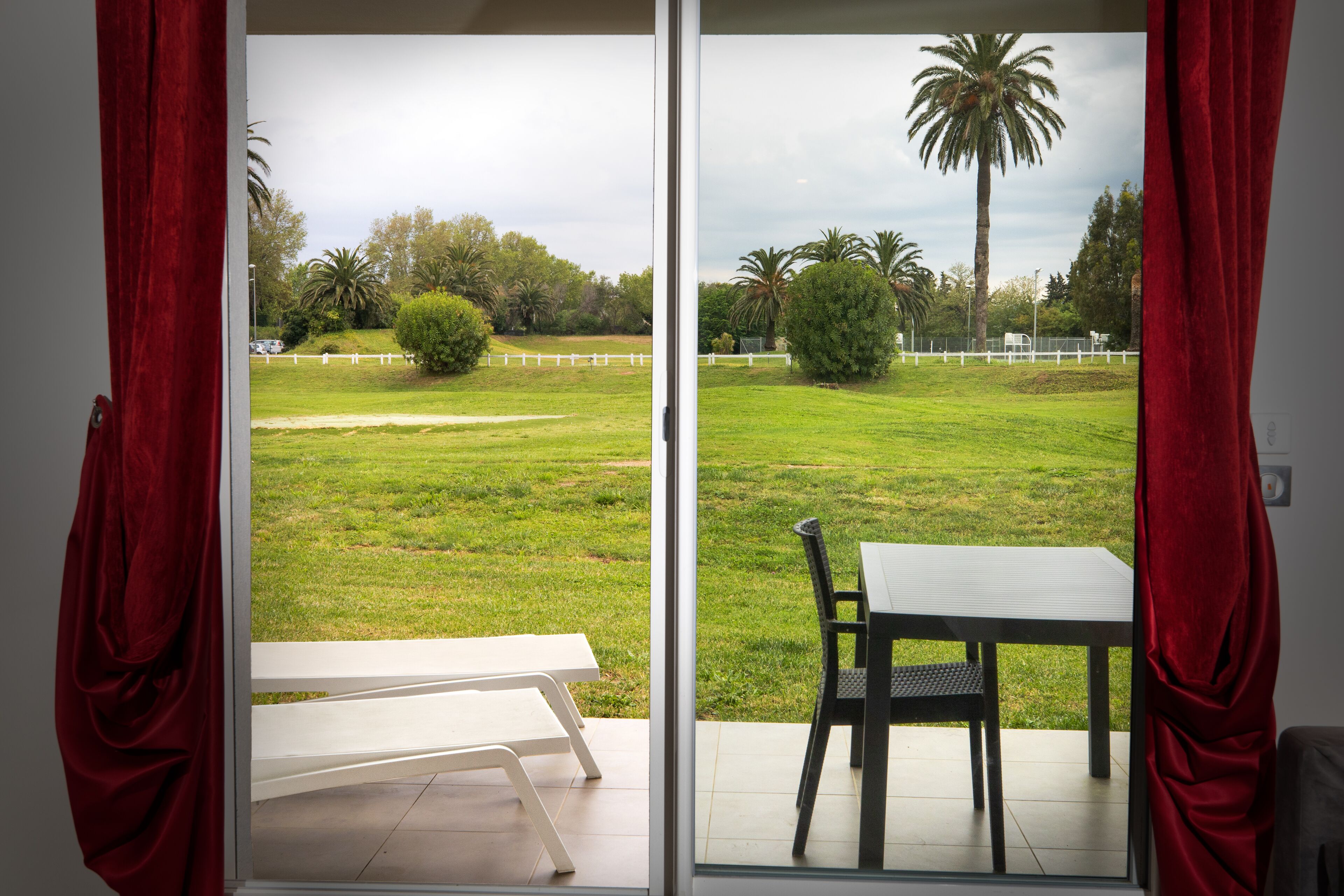 A room with a sliding glass door leading to a grassy outdoor area with a white table and chair.