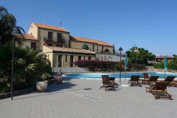A resort with a swimming pool, lounge chairs, and a large building with a tiled roof.