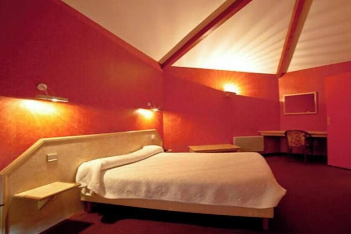 A single bed with a headboard, a desk, a chair, and a wall-mounted TV in a room with red walls and a slanted ceiling.