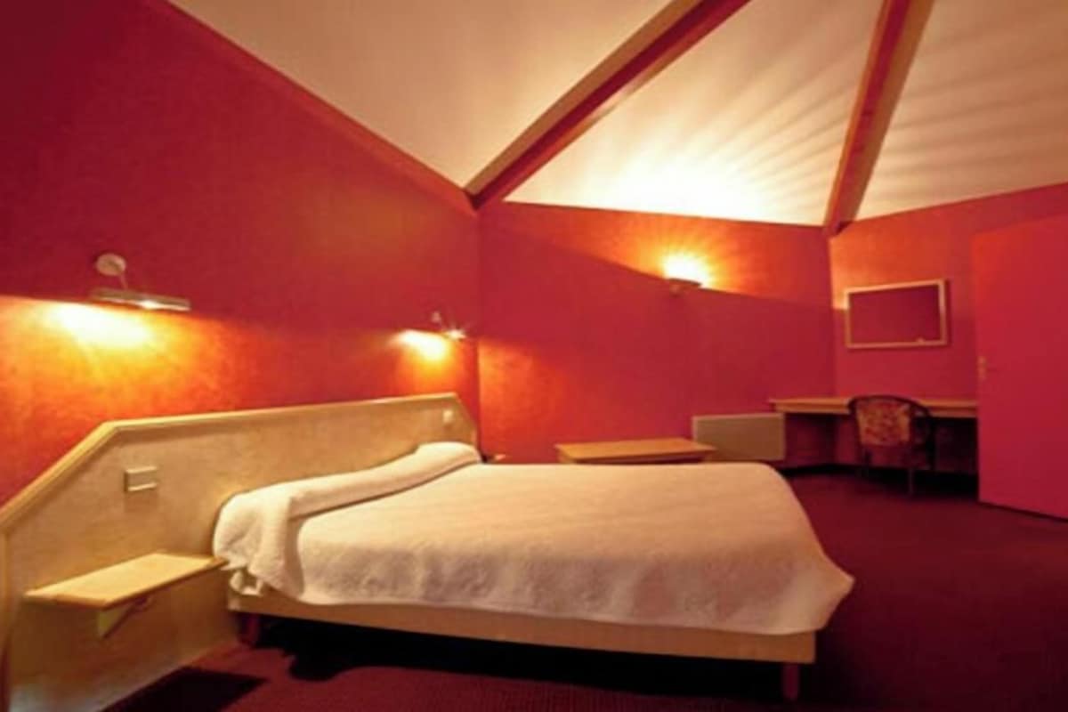 A room with a bed, bedside table, and a desk with a chair.
