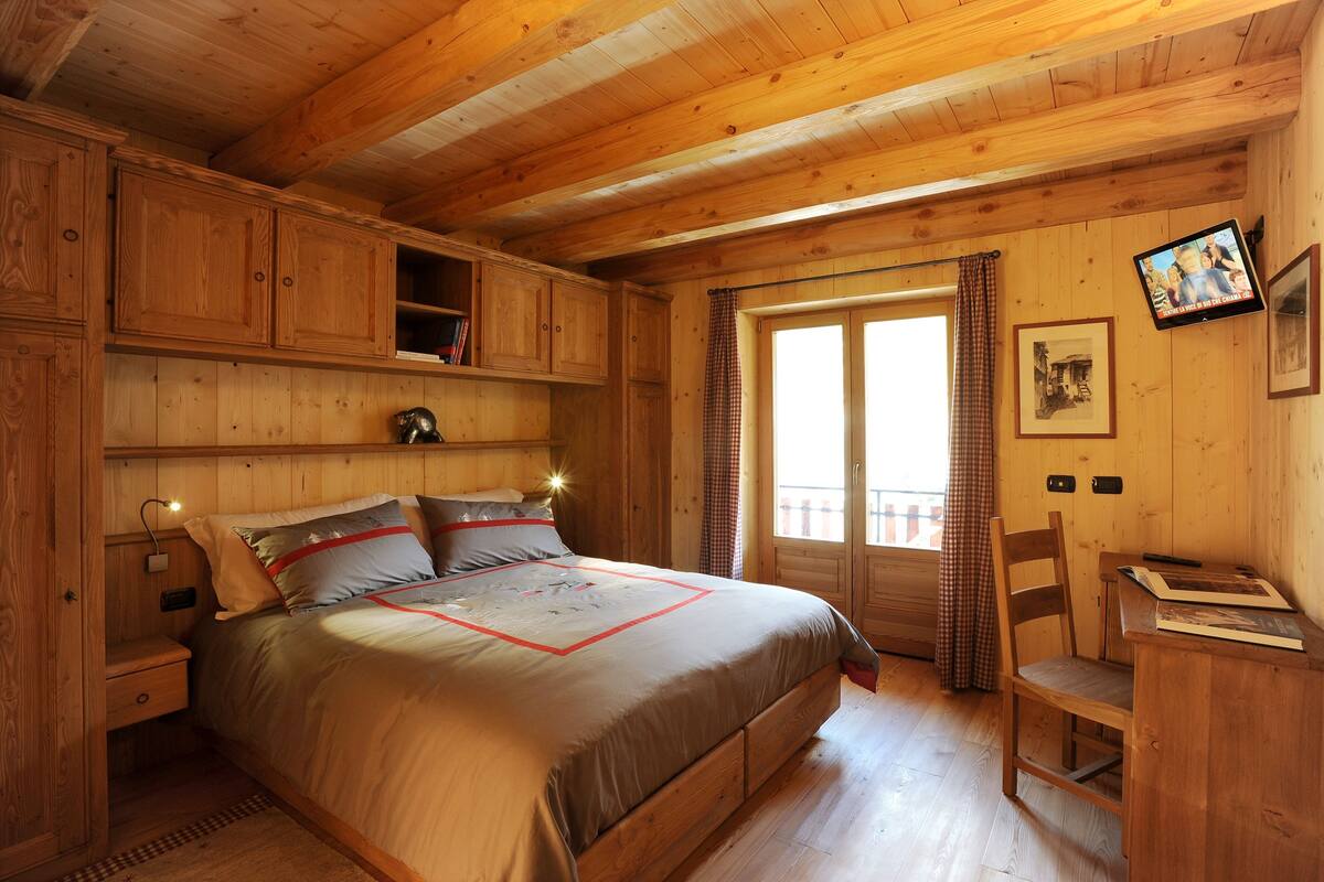A wooden cabin bedroom with a bed, a desk, and a television.