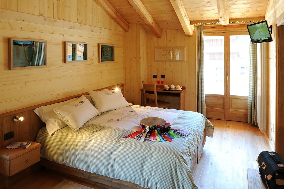 A wooden cabin bedroom with a bed, nightstands, a desk, and a television.