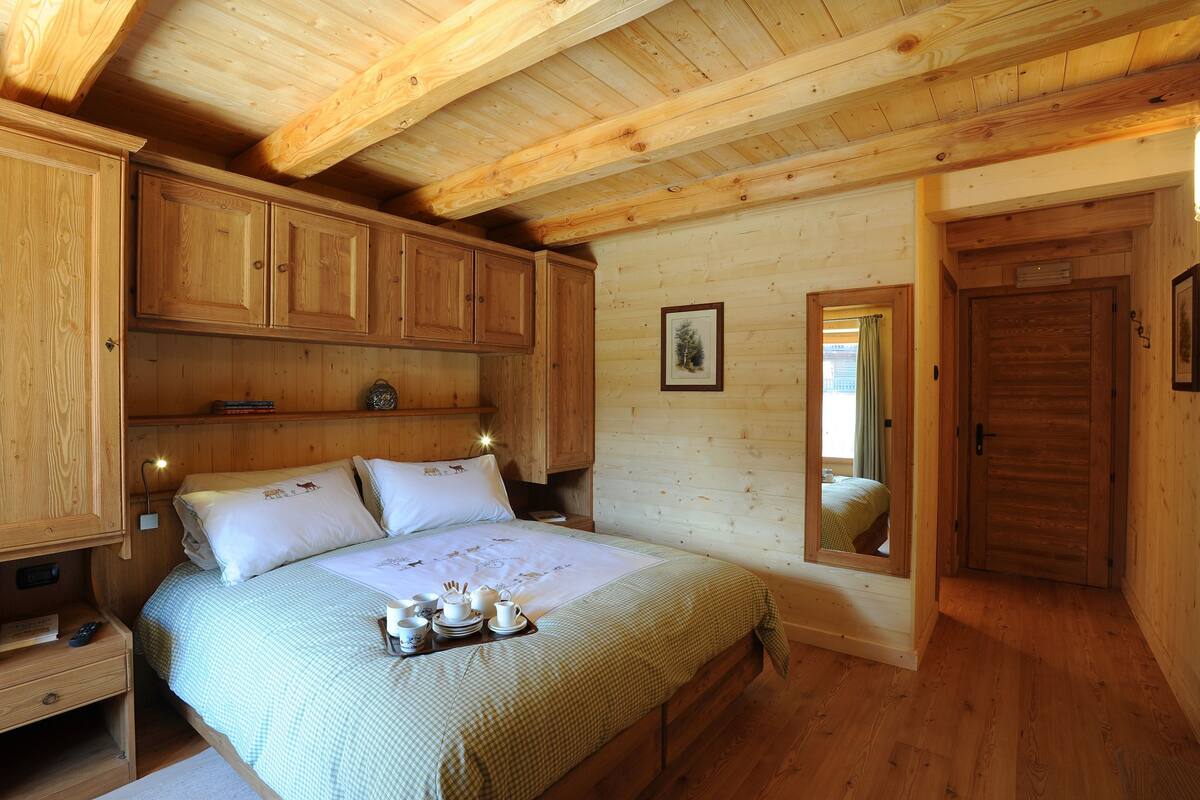 A wooden cabin bedroom with a bed, nightstands, and a wooden wardrobe.