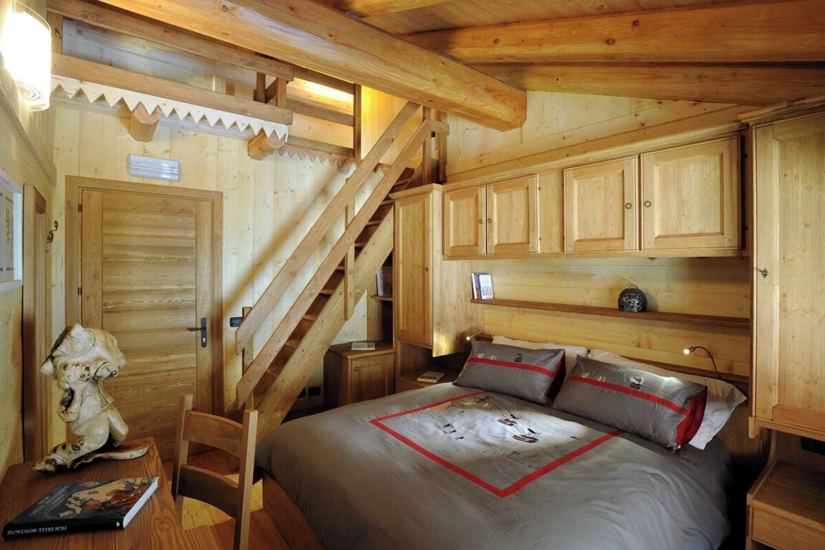 A wooden cabin room with a bed, a staircase, and wooden cabinets.