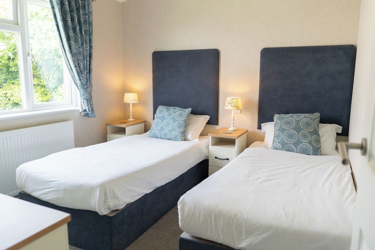 A hotel room with two single beds, each with a headboard, bedside tables, and lamps.