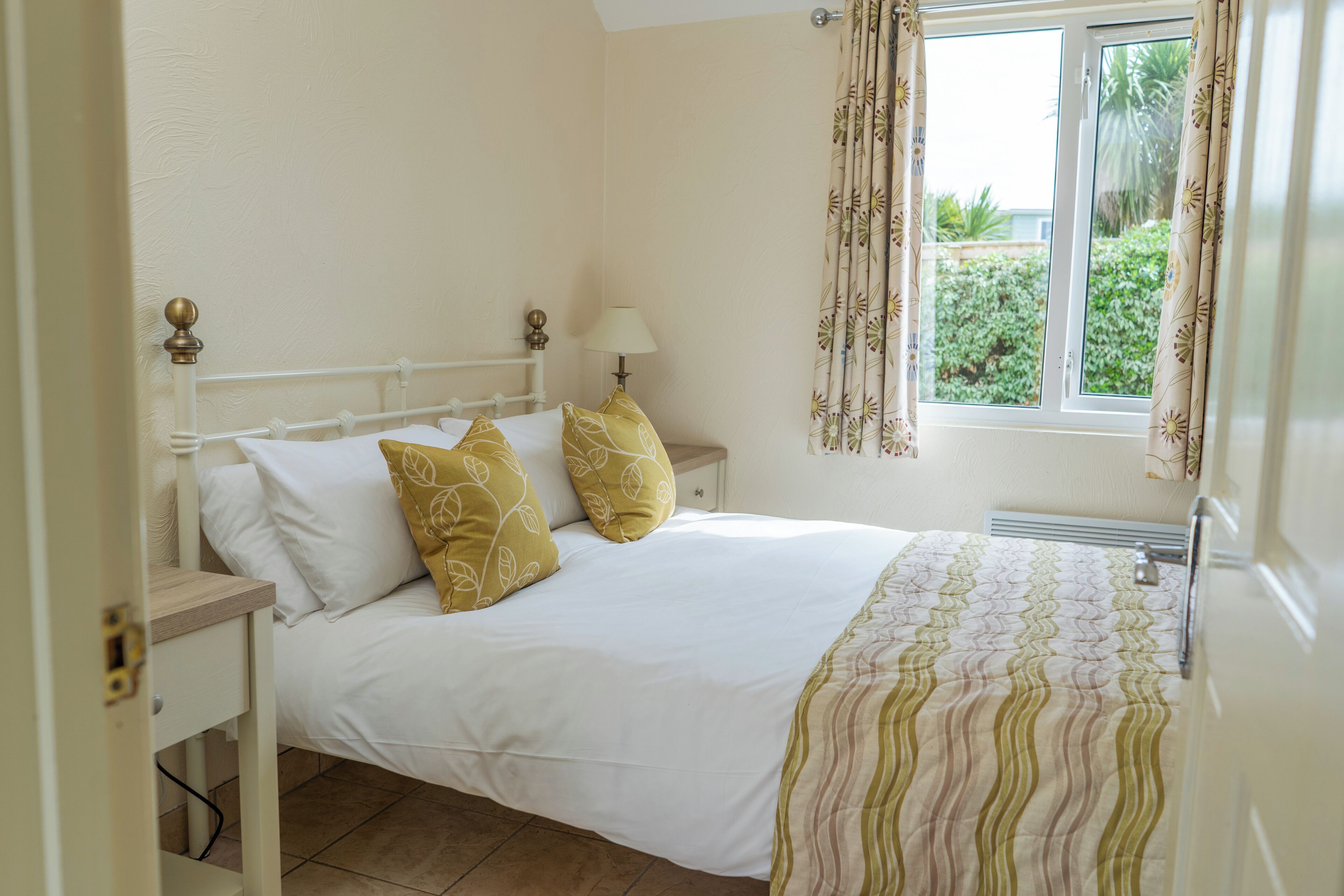 A neatly made bed with white and yellow pillows, a bedside lamp, and a window with curtains.