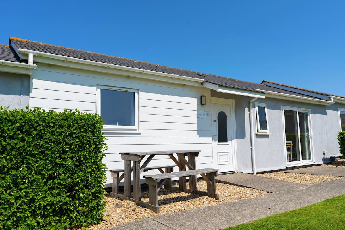 A white mobile home with a picnic table in front, a small garden, and a clear blue sky.