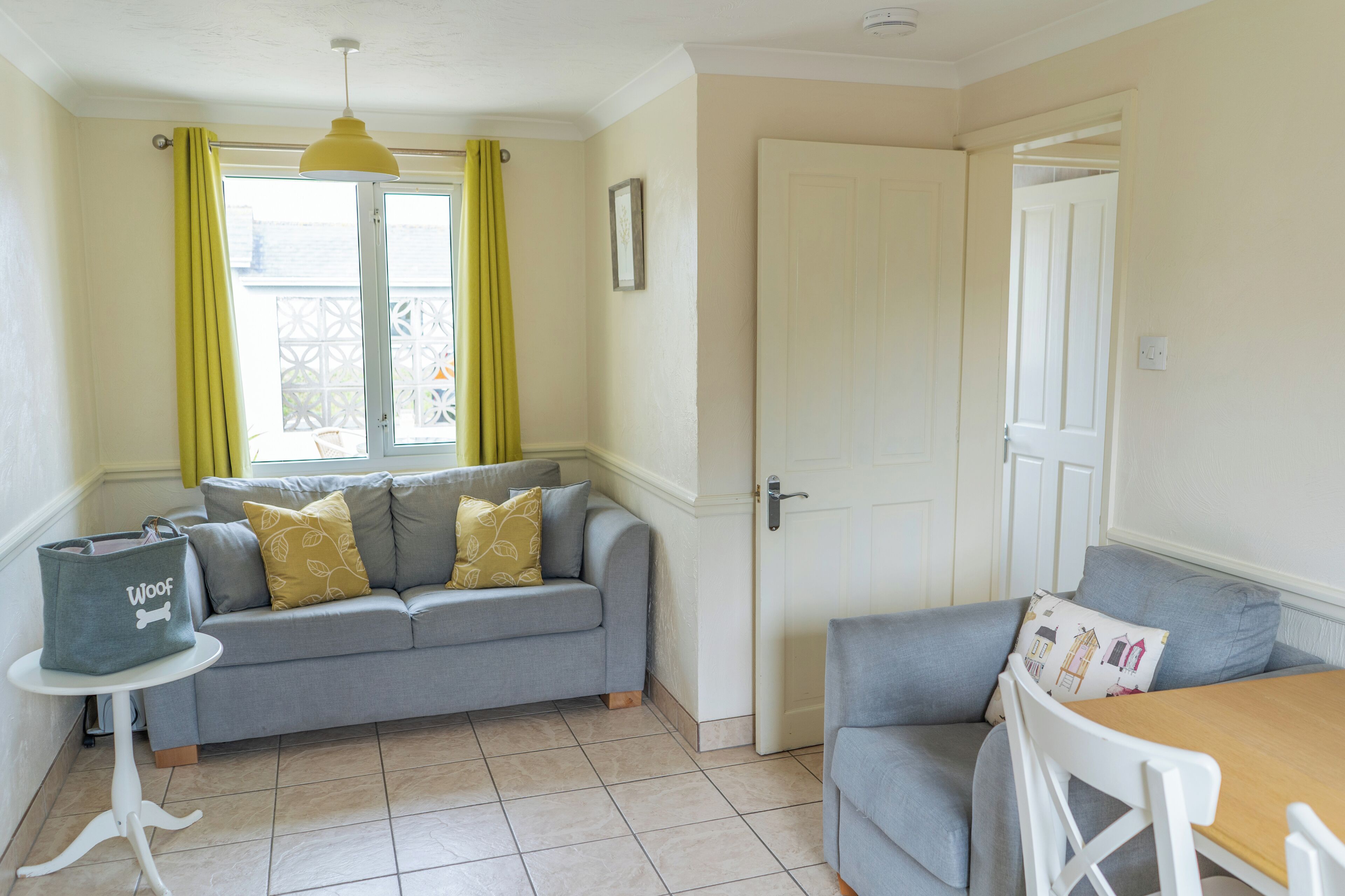 A cozy room with a grey sofa, a small table, and a window with yellow curtains.