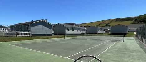 A tennis court with a net, surrounded by buildings and a clear sky.