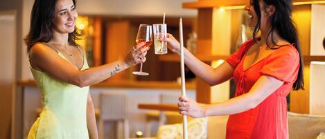 Two people toasting with drinks in a room with a pool table, a sofa, and a lamp.
