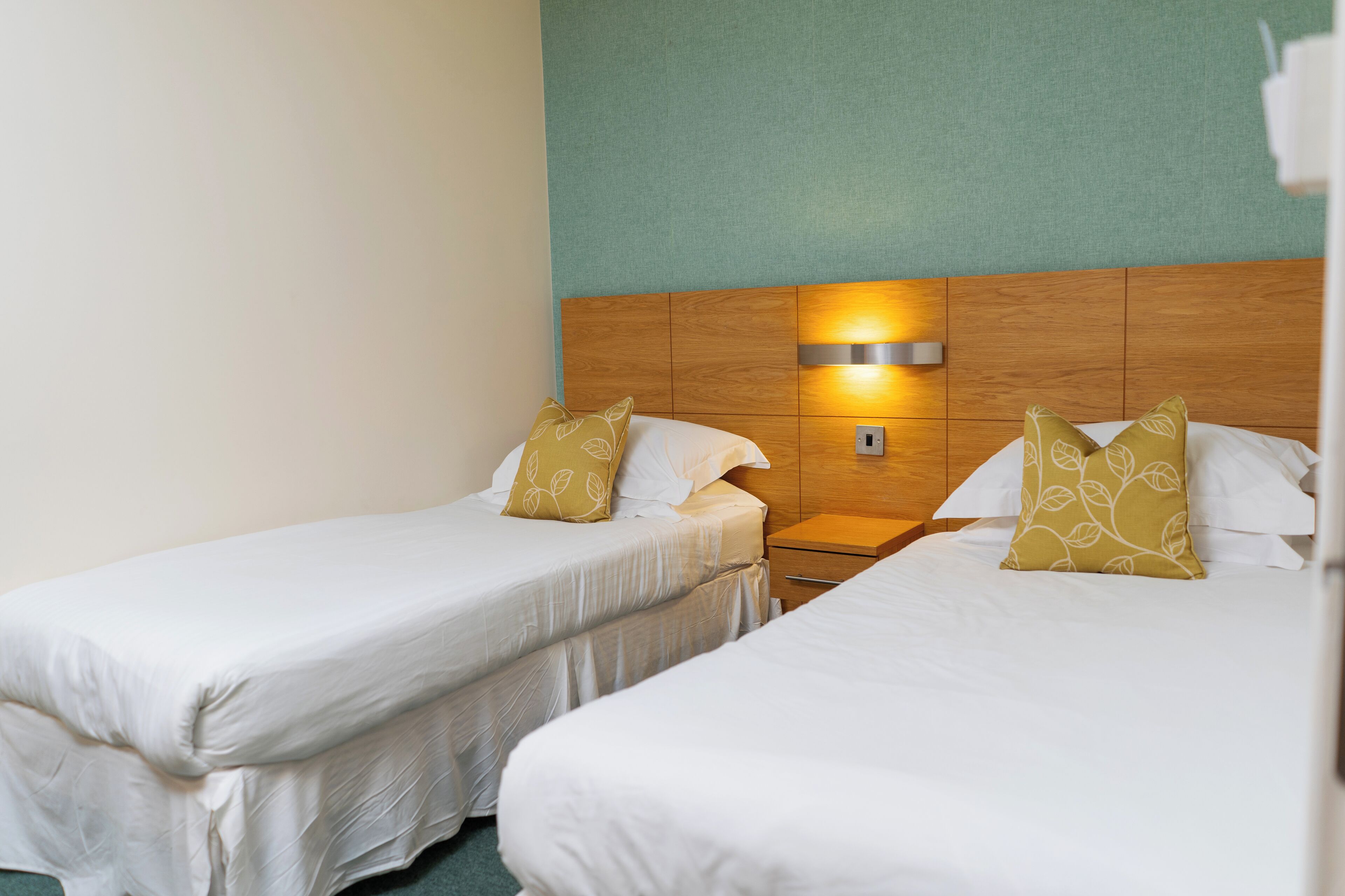 A hotel room with two single beds, each with white bedding and decorative pillows.