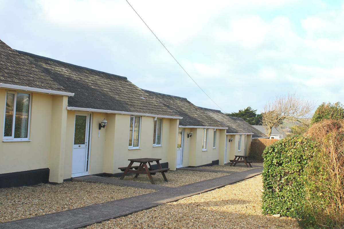 A row of yellow cottages with picnic tables and a gravel path.
