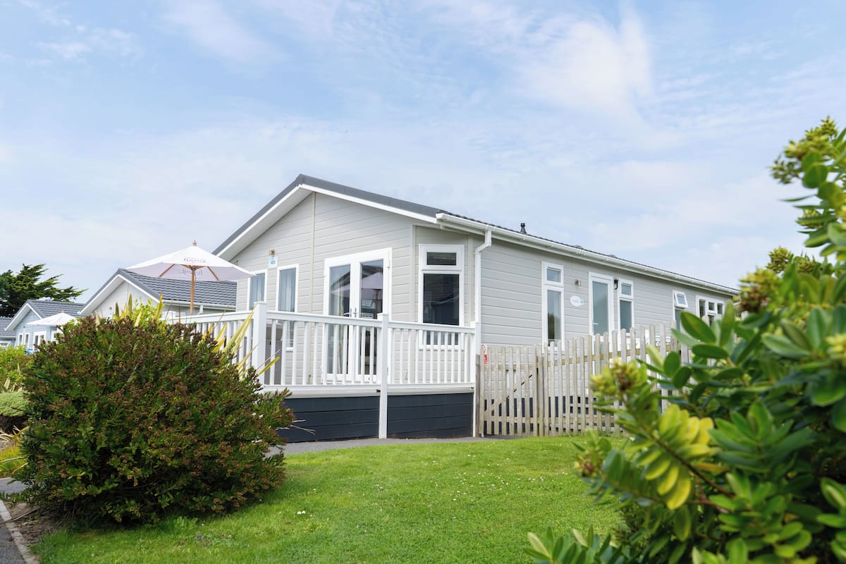 A single-story mobile home with a white exterior, a fenced front yard, and a small garden area.