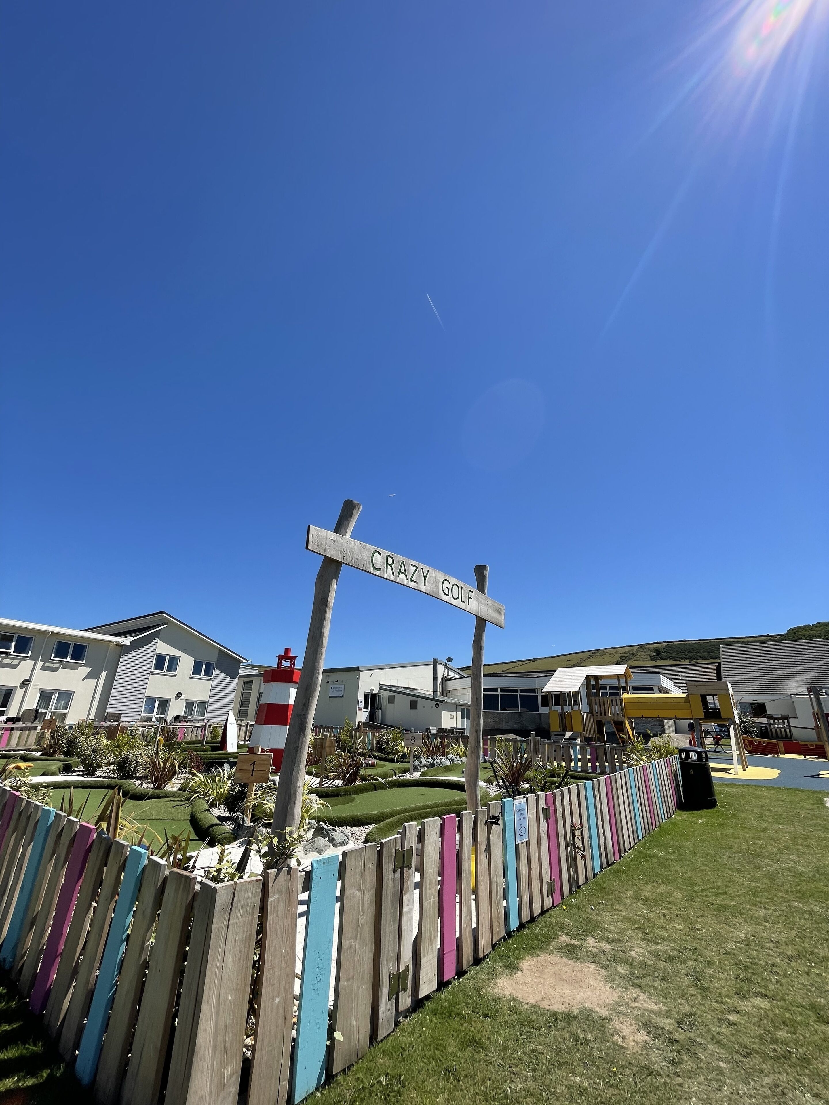 Un cartel que dice 'CRAZY GOLF' en una zona residencial con casas y un parque infantil.