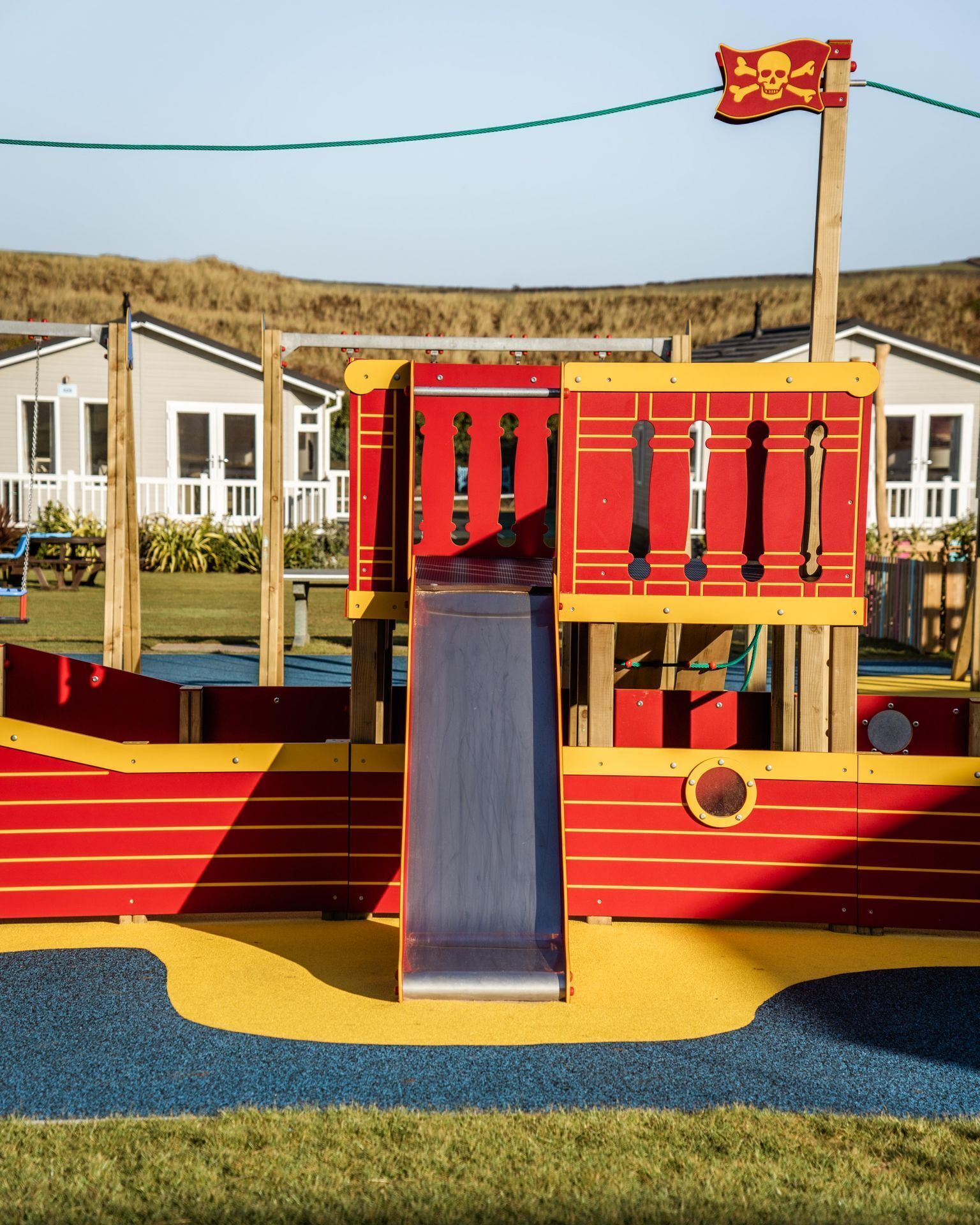 A playground with a slide and climbing structures, surrounded by a grassy area and a building in the background.
