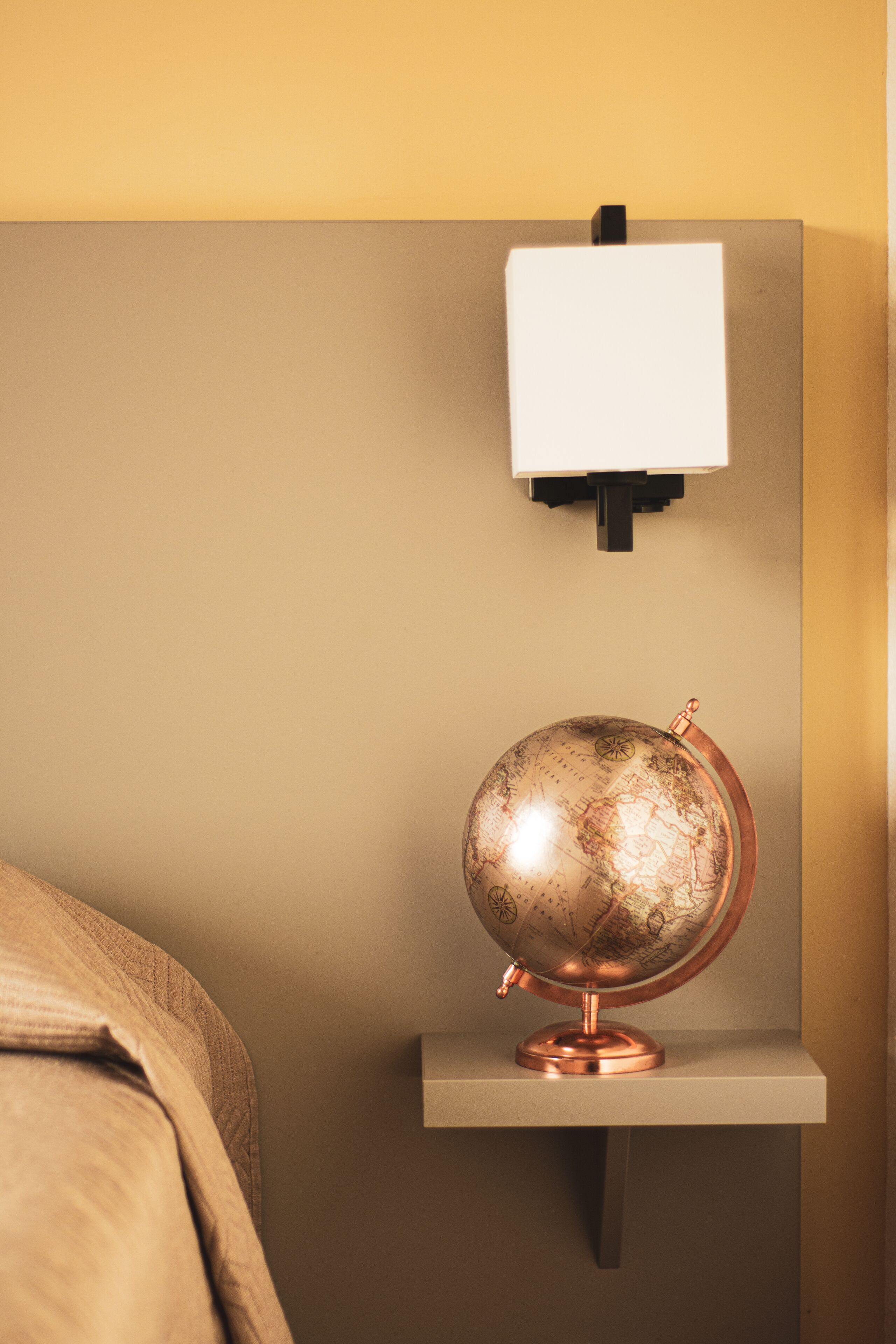 A globe on a shelf with a wall-mounted light above it.